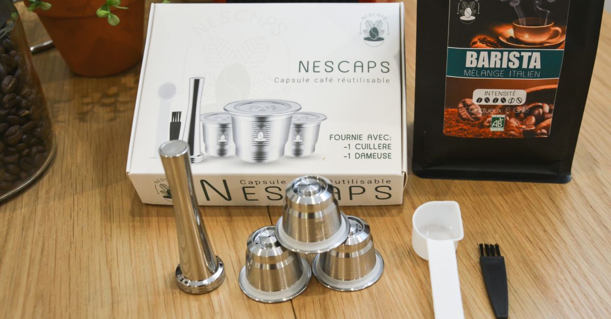 La capsule réutilisable Nescaps en acier inoxydable, fournie avec une cuillère et une dameuse, aux côtés d'un café barista mélange italien